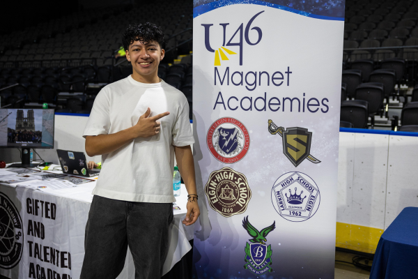  A boy stands and points next to a sign that reads U-46 Magnet Academies